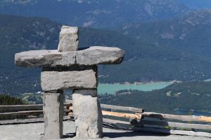 A stone inukshuk sculpture standing against a stunning mountain backdrop at the top of Whistler Mountain. This iconic landmark is a popular stop for visitors taking the Peak 2 Peak gondola.