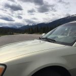 A gold SUV parked at a scenic viewpoint along the Icefields Parkway, with snow-capped peaks and forested hills in the distance&mdash;perfect example of BC road trip terrain from Vancouver toward the Rockies.