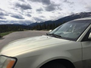 A gold SUV parked at a scenic viewpoint along the Icefields Parkway, with snow-capped peaks and forested hills in the distance&mdash;perfect example of BC road trip terrain from Vancouver toward the Rockies.