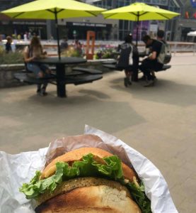 A veggie burger wrapped in paper, held up in front of outdoor picnic tables under bright yellow umbrellas. Whistler Village is filled with great spots to grab a bite after a day of exploring.
