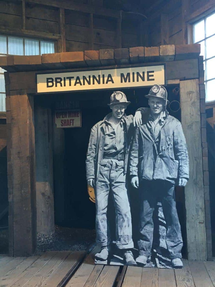A wooden mine entrance labeled “Britannia Mine” features a life-size cutout of two smiling miners in vintage uniforms. The display creates a photo-worthy moment that introduces the underground tour with a touch of personality and history.