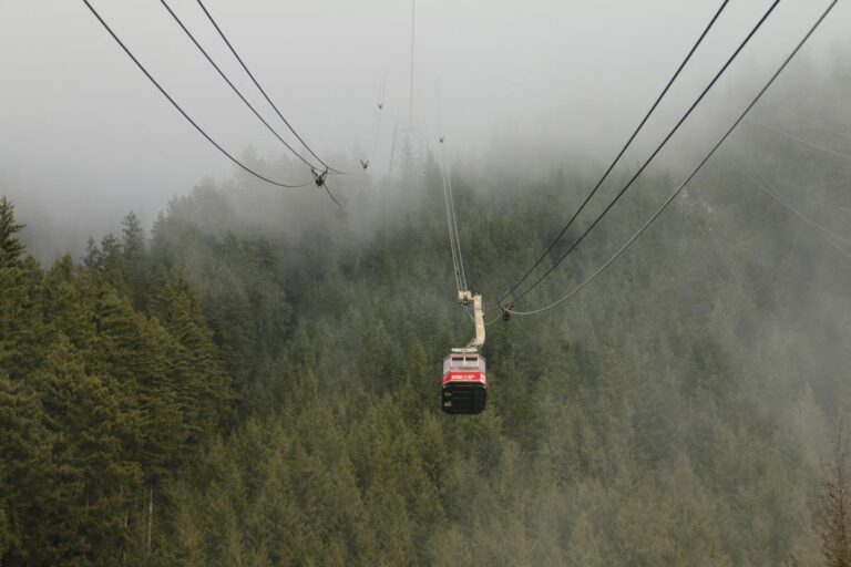 A scenic gondola ride through dense forest and mist, showcasing the iconic Grouse Mountain Skyride cable car surrounded by towering evergreens.