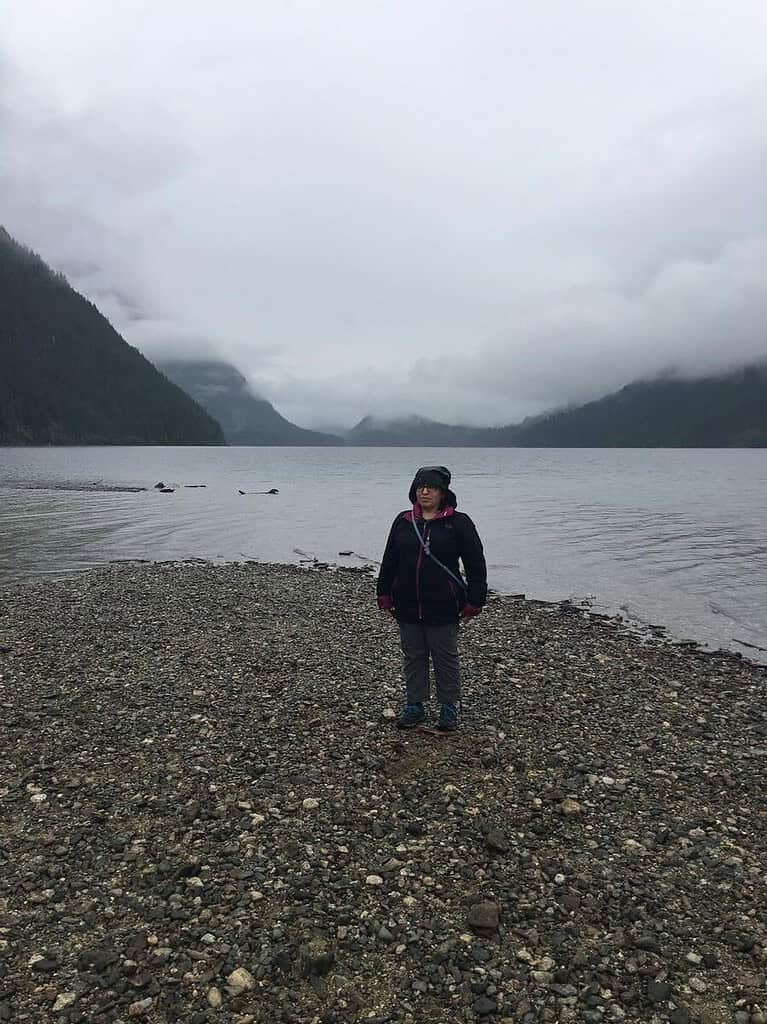Tazim Damji standing on the rocky shore with mountains and dark clouds in the background.