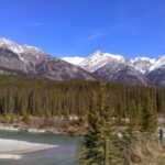 A breathtaking view of a rugged mountain range with a winding river and a partially frozen riverbed in the foreground.