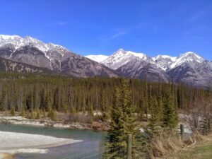 A breathtaking view of a rugged mountain range with a winding river and a partially frozen riverbed in the foreground.