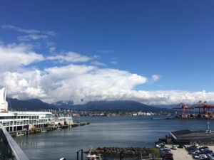 Panoramic view of downtown Vancouver and the North Shore Mountains from Canada Place, with port cranes and cruise terminals visible&mdash;a scenic starting point for any Vancouver road trip or coastal drive.