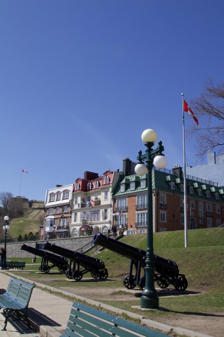 Row of cannons lined up on Dufferin Terrace, with colorful historic buildings and Canadian flags fluttering in the background under a bright blue sky. This scenic spot near Château Frontenac is a must for photos that blend history, color, and charm in one shot.