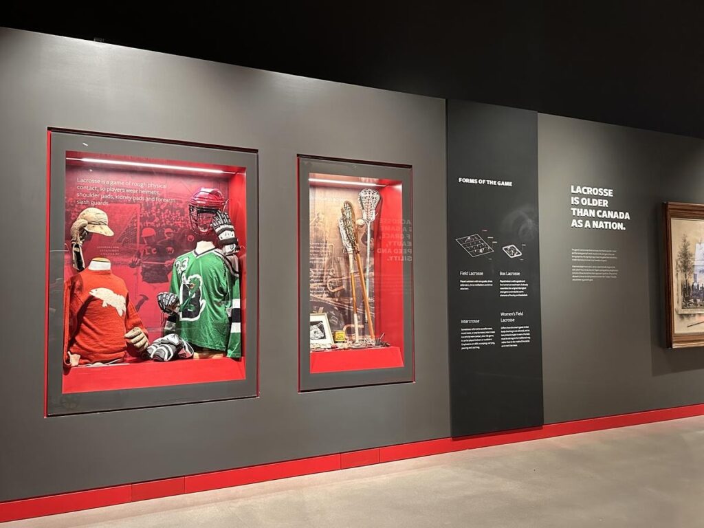Display at the Canadian Lacrosse Hall of Fame featuring vintage jerseys, lacrosse sticks, helmets, and historic information panels. Visiting the Hall of Fame adds a fun and educational stop that’s all about Canada’s national summer sport.