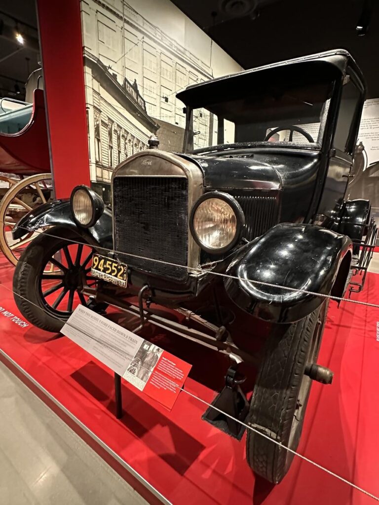 A black vintage Model T car displayed inside a museum, surrounded by bright red exhibit panels and historic signage. Unique artifacts like this make the local museums in New Westminster extra interesting to explore.