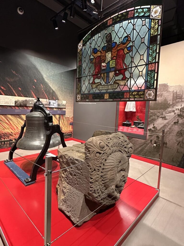 Museum exhibit featuring a colorful stained-glass window, a carved stone artifact, and an old metal bell. Pieces like these show how much rich and fascinating history is packed into New Westminster’s downtown museums.