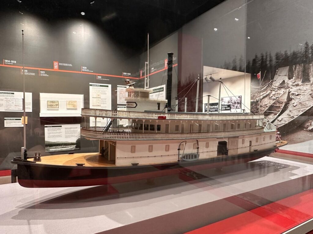 Model of a historic riverboat displayed in a museum case, surrounded by photos and information panels about river history. Adds a glimpse into New Westminster’s deep connection to the Fraser River and early transportation.