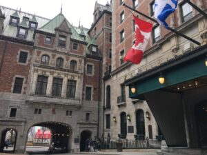 Courtyard and main entrance of the Ch&acirc;teau Frontenac, with flags waving above and people gathered near the historic stone archway. It&rsquo;s a great visual intro to the grandeur of the hotel and its old-world European feel.