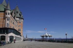 View of Ch&acirc;teau Frontenac and the Dufferin Terrace boardwalk on a sunny day, with a Canadian flag waving above a green-and-white striped gazebo.