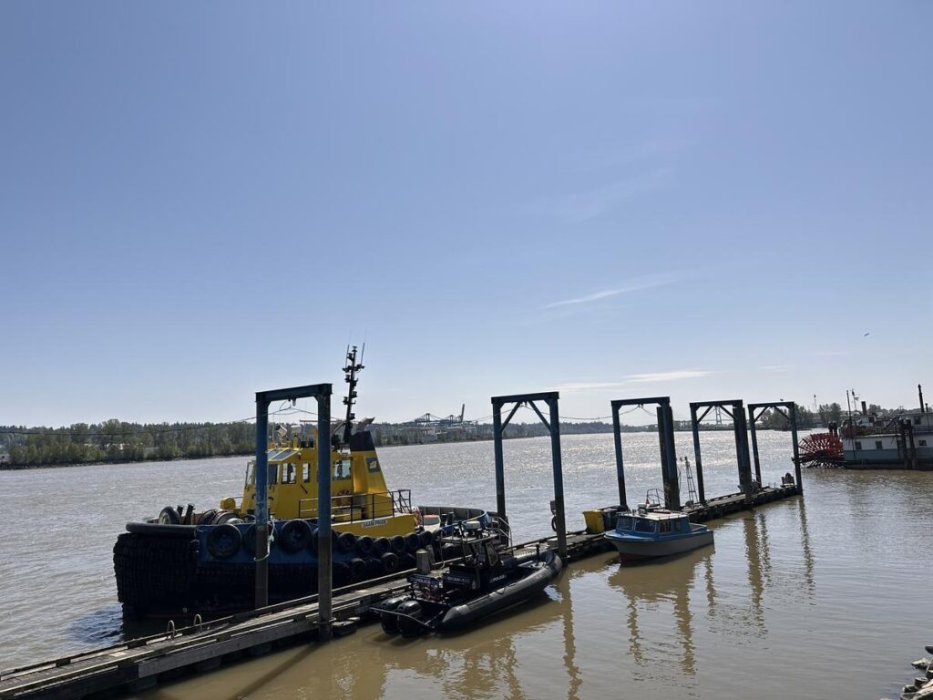 Small dock with a bright yellow tugboat and a few smaller boats floating on the Fraser River under a sunny sky. Brings in the working river life that’s still a big part of downtown’s identity.