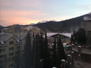 Soft pastel light glows over the rooftops of Whistler Village with Blackcomb Mountain in the distance, seen from a Westin Whistler room. Watching the sun rise over the mountains is one of the quiet perks of a stay at this central Whistler resort.