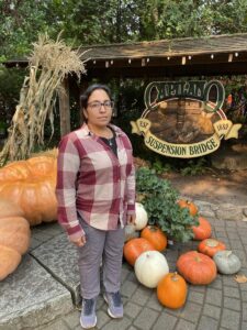 Woman wearing a red plaid button-up and grey pants poses by a pumpkin display at Capilano Suspension Bridge&mdash;casual outfit for fall in Vancouver, Canada.