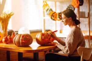 A woman in a cozy cable-knit sweater sits at a wooden table carving a jack-o'-lantern, surrounded by autumn-themed decorations and warm afternoon light. Fall in Vancouver brings festive moments like these indoors, where sweaters and seasonal crafts are just as much a part of the experience as outdoor adventures.