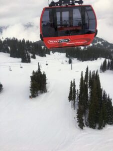 A red Peak 2 Peak gondola cabin glides high above snowy ski slopes and dense evergreen forest at Whistler Blackcomb, showcasing one of the top things to do in Whistler, BC in winter.