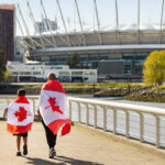 Two fans draped in Canadian flags walking along False Creek towards BC Place stadium in Vancouver during World Cup 2026.