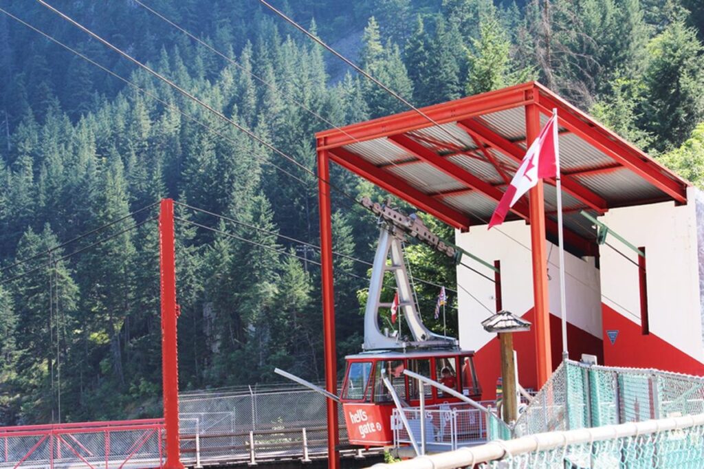 Red Hell&rsquo;s Gate Airtram parked at the lower station with cables, flags, and forest-covered mountains in the background.