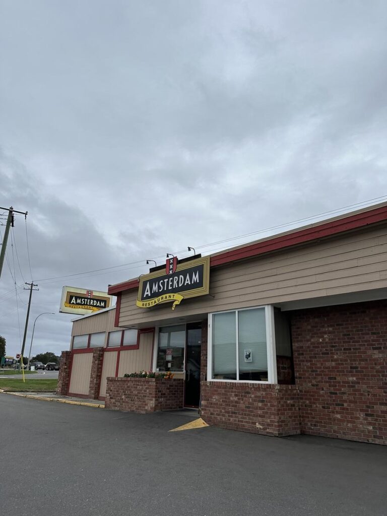 Exterior of Amsterdam Restaurant in Kamloops with a red-and-beige building and a sign hanging above the entrance.