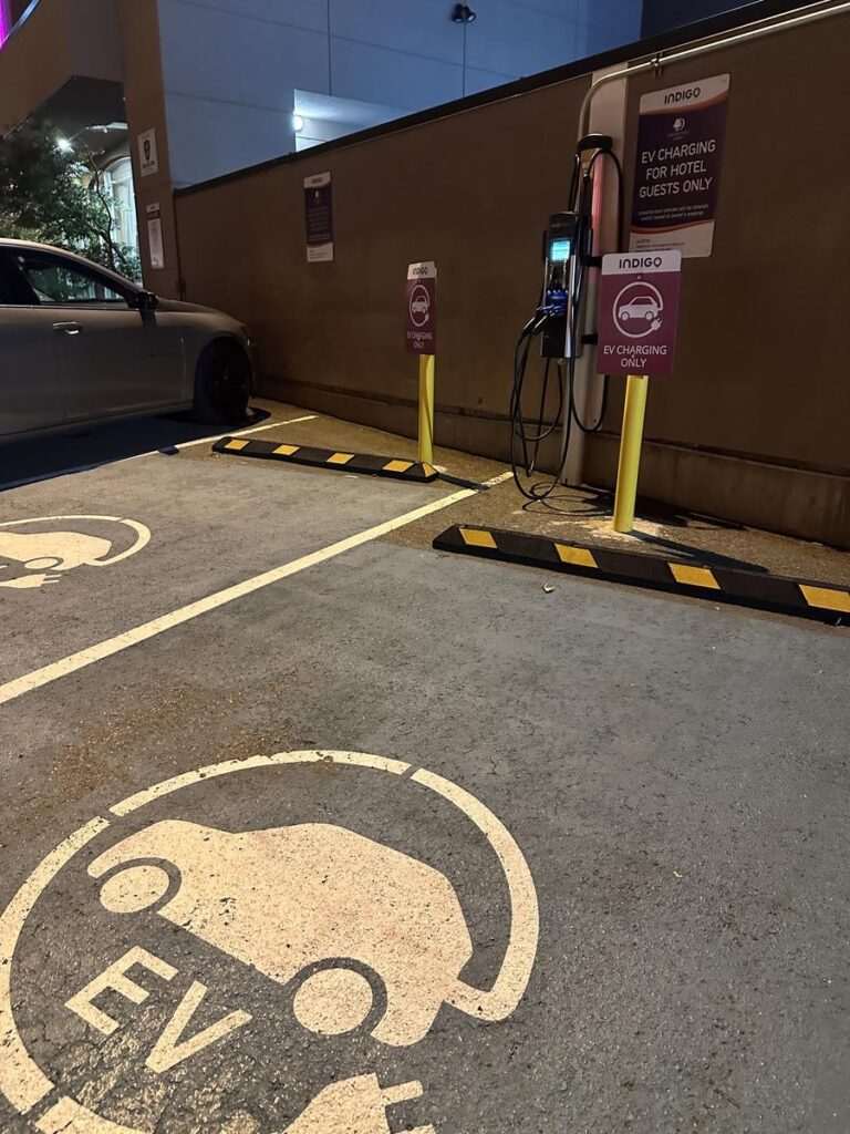 EV charging station with a charging cable mounted on a wall between two clearly marked electric vehicle parking spots at night.