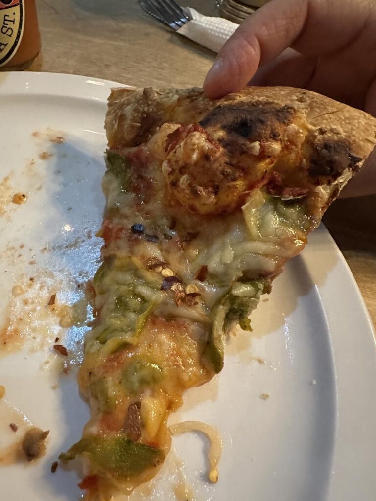 Close-up of a single slice of vegan pizza topped with green peppers, onions, and melted cheese on a white plate.