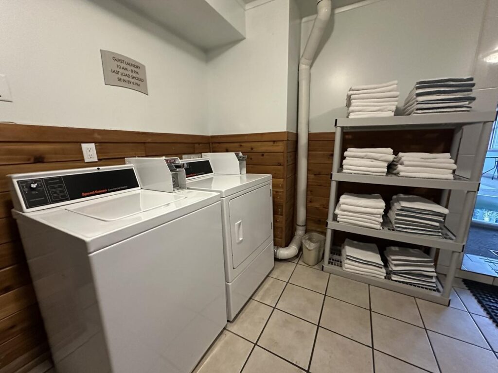 Hotel laundry room featuring Speed Queen washer and dryer machines next to organized shelves stocked with clean white towels.