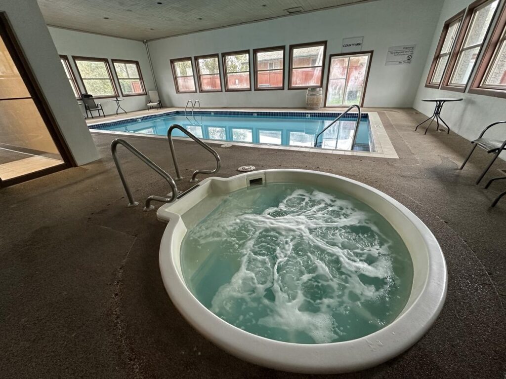 Indoor pool area at Quality Inn Vernon with large rectangular swimming pool and bubbling round hot tub surrounded by lounge chairs and windows.