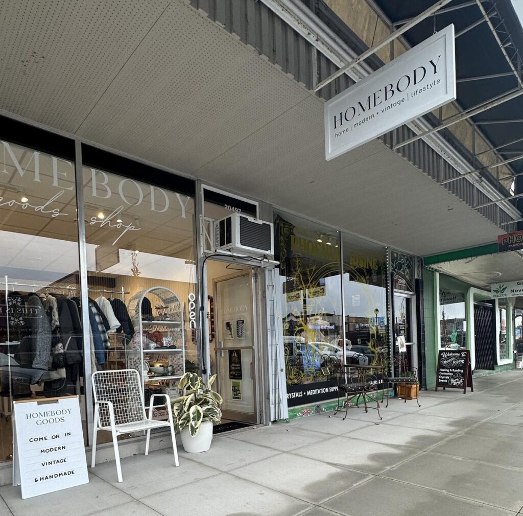 The storefront of Homebody, a modern lifestyle and vintage goods shop in Langley City, showing a welcoming display with outerwear, plants, and a sidewalk sign that reads &ldquo;Modern, Vintage & Handmade.&rdquo;