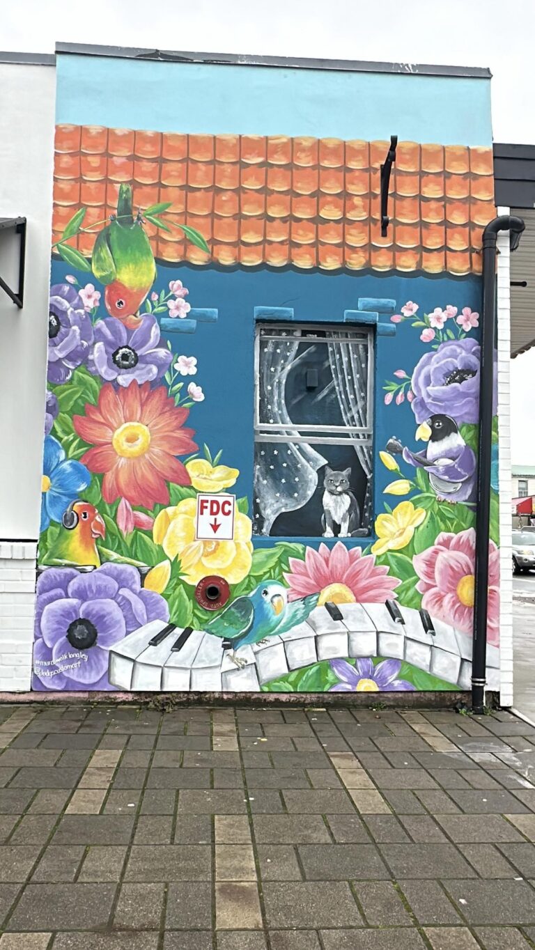 A whimsical mural filled with colorful flowers, tropical birds, and a cat looking out from a curtained window, with a piano keyboard winding along the bottom.