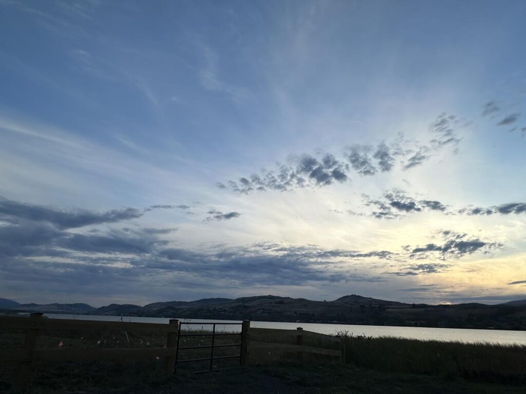 Soft evening light reflects off Swan Lake in Vernon, BC, with streaks of clouds catching the last golden tones of sunset above rolling Okanagan hills.
