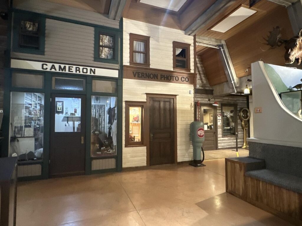 Recreated historic storefronts inside the Vernon Museum, including &ldquo;Cameron&rdquo; and &ldquo;Vernon Photo Co,&rdquo; with wood facades and vintage displays.