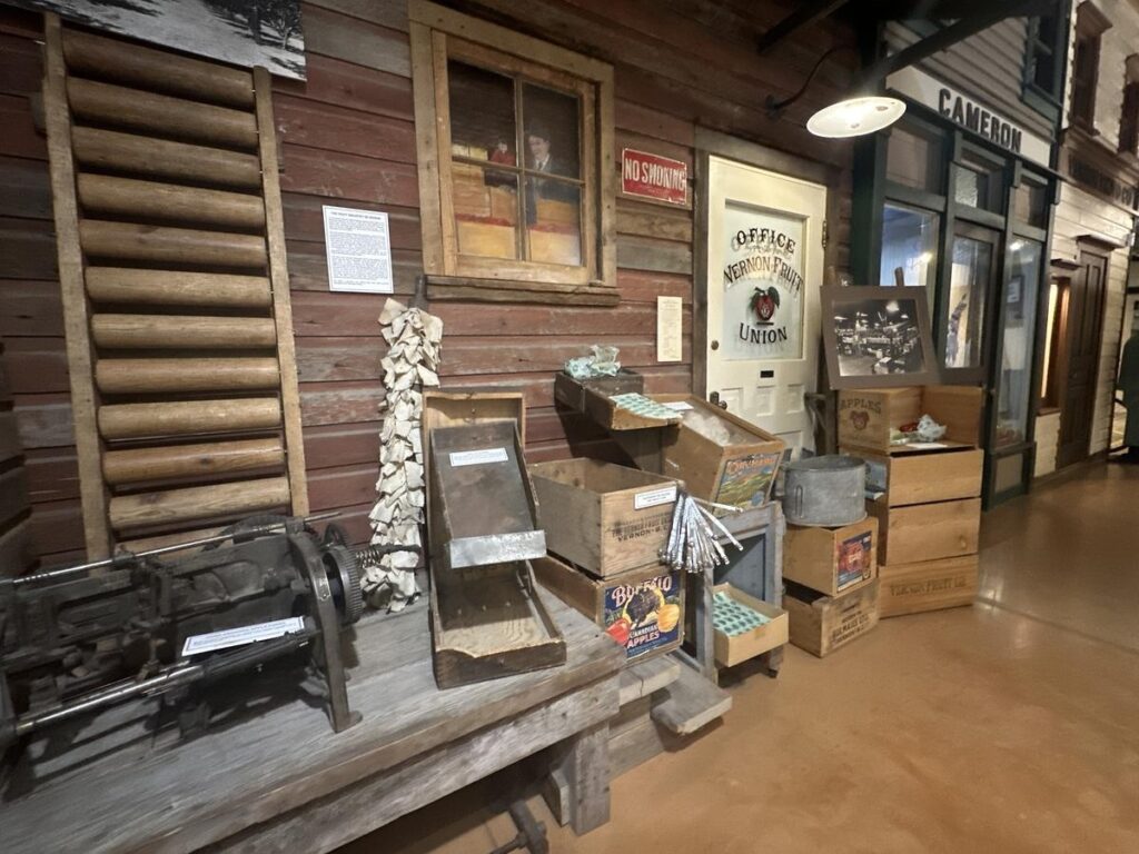 Historic display at the Vernon Museum showing crates, tools, and packaging from the Vernon Fruit Union&rsquo;s heyday, with a vintage office door and &ldquo;no smoking&rdquo; sign.