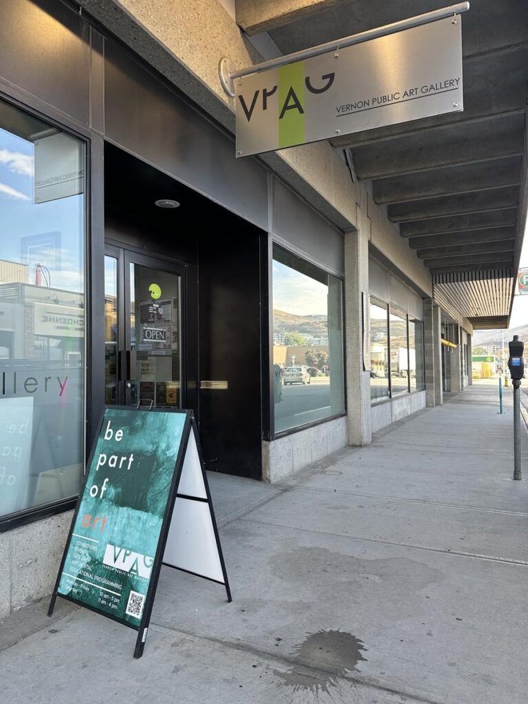 Street-level view of the Vernon Public Art Gallery entrance with a sandwich board that reads &ldquo;be part of art,&rdquo; and a modern sign reading VPAG on the building.