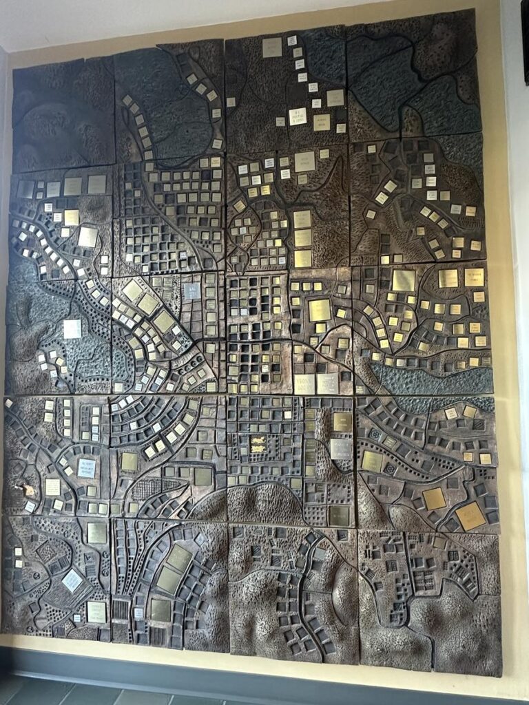 A sculpted bronze relief map mounted on a wall, representing an aerial view of Vernon&rsquo;s street layout with raised sections and labelled blocks.