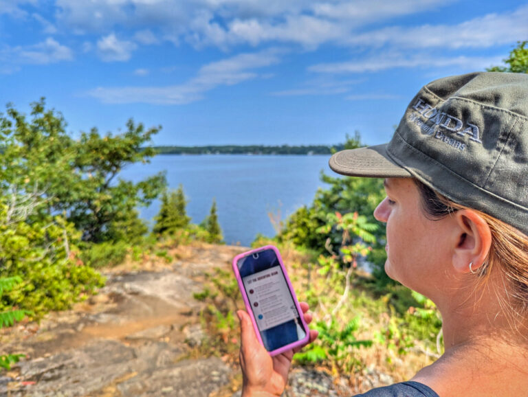 Lady holding a phone in front of a view of the lake