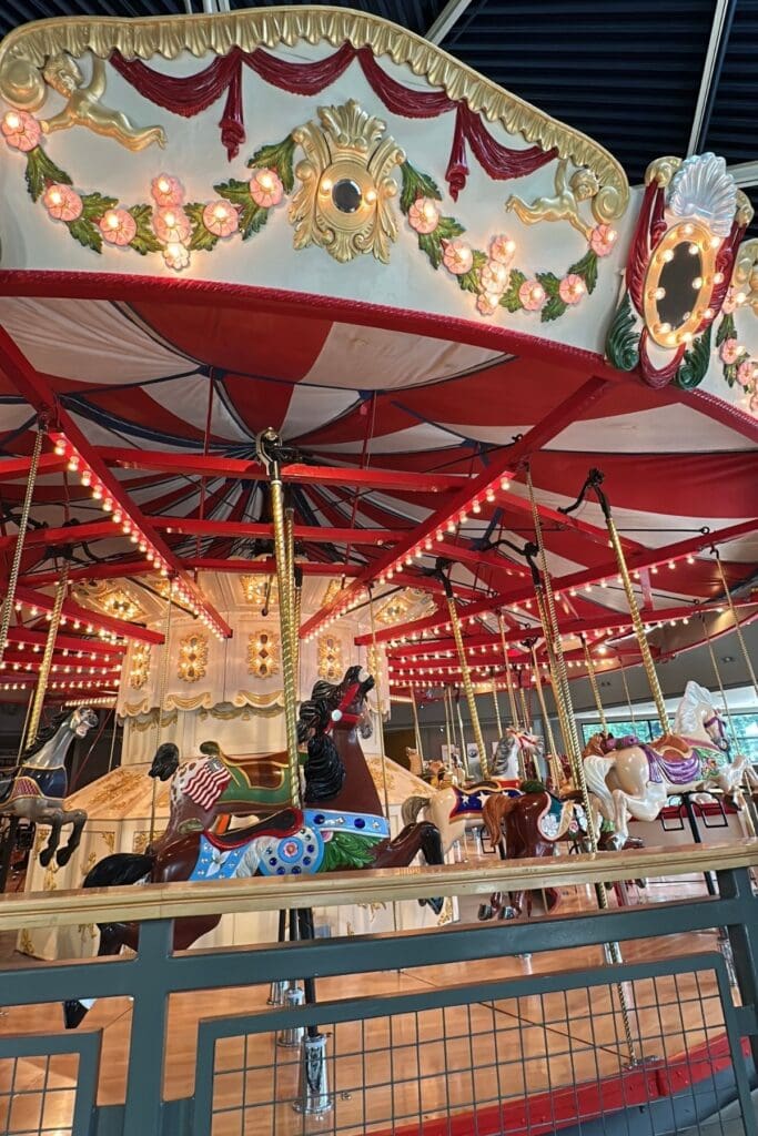 The ornate 1912 carousel inside Burnaby Village Museum, with hand-carved and painted horses, a red and white striped canopy, gold decorative trim, cherub details, and string lights, Burnaby, BC.