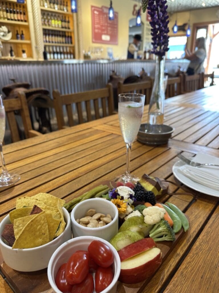 Vegan charcuterie board with fresh vegetables, fruit, corn chips, nuts, edible flowers and dark chocolate on a wooden tray at Krause Berry Farms in Langley, alongside a sparkling water glass and a vase of purple lupins