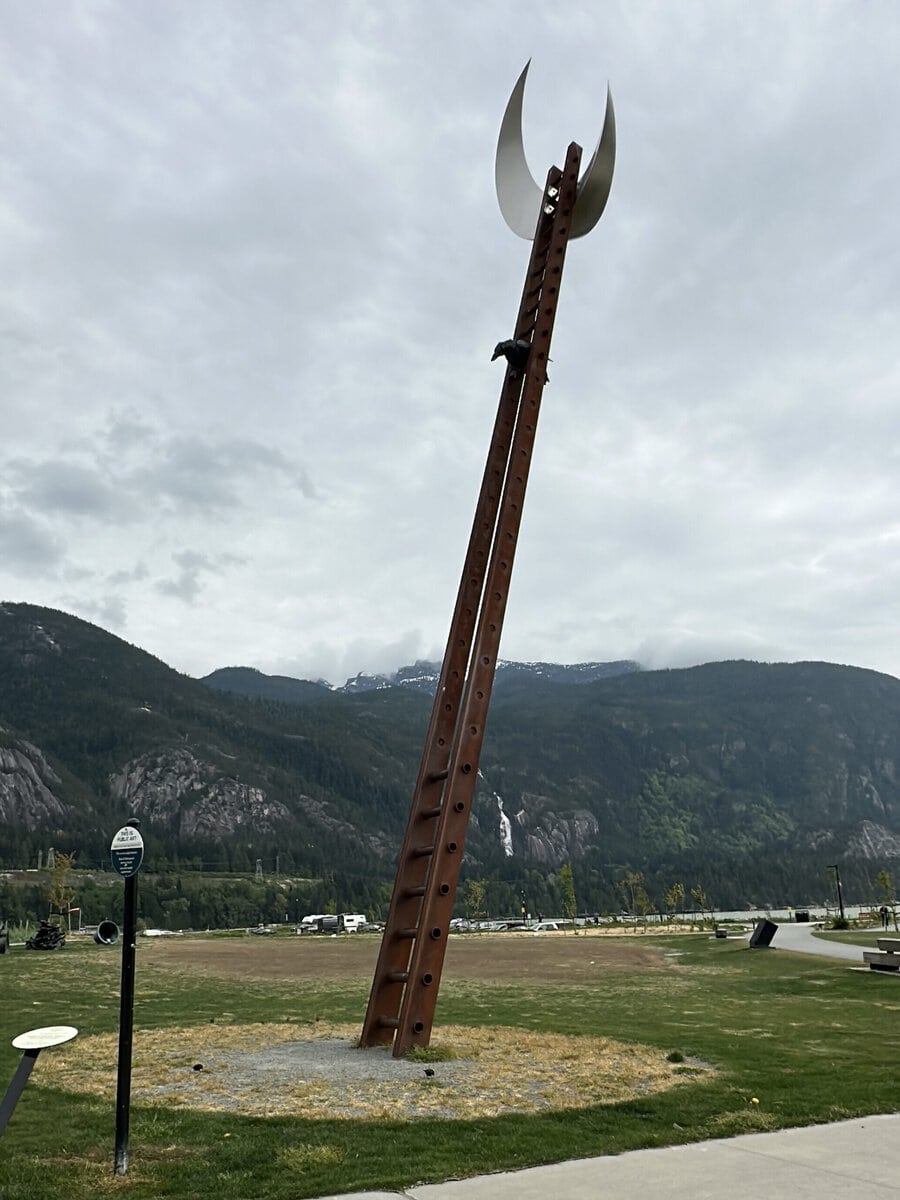 Tall public art sculpture at Sp'&aacute;kw'us Feather Park in Squamish, BC, with mountain views, open paths, and soft adventure scenery.