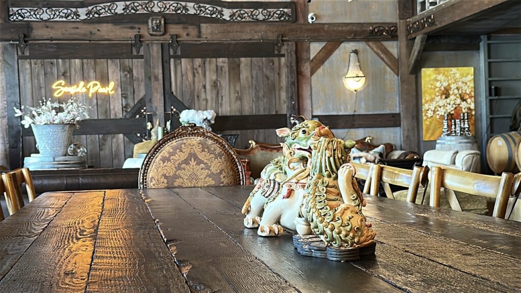 Rustic barn-style tasting room interior at Seaside Pearl Winery in Abbotsford with a heavy wooden farm table, ceramic foo dog statue, ornate chair, exposed beams and eclectic decor