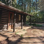 The front porch and log exterior of the Murdo Frazer cabin set in a conifer forest at Capilano River Regional Park, North Vancouver, BC