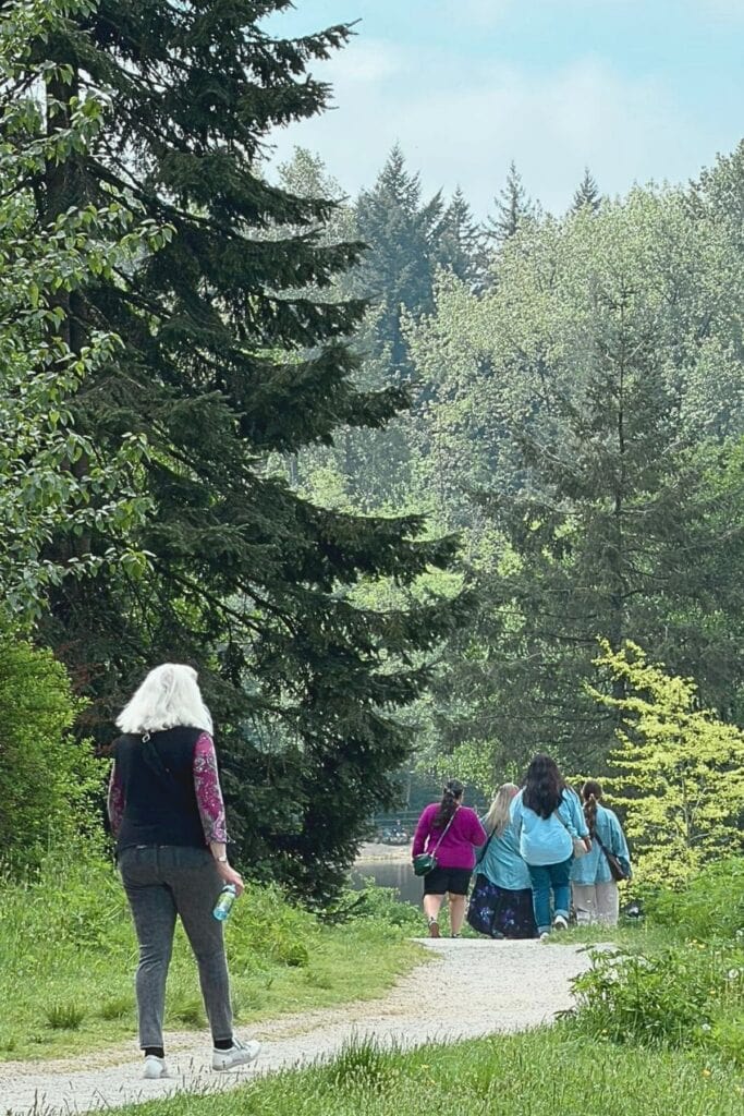 Visitors walking along a gravel trail through Green Timbers Urban Forest in Surrey BC surrounded by towering conifers and lush spring foliage