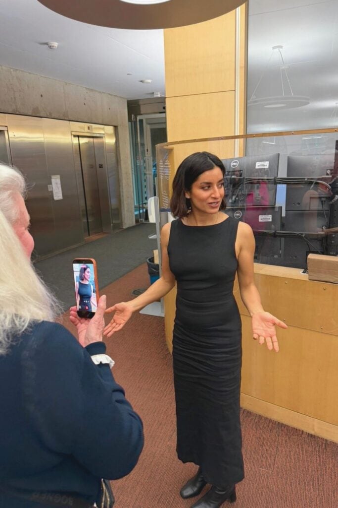 Supinder Wraich gesturing inside the Surrey City Hall library area while a visitor films her on a smartphone during a behind-the-scenes tour in Surrey BC