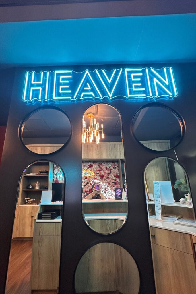 Bright blue neon HEAVEN sign above a wall of oval mirrors reflecting the reception area of Heaven Sushi + Sake Bar. The restaurant is located inside Best Western Premier Aberdeen Kamloops in BC.