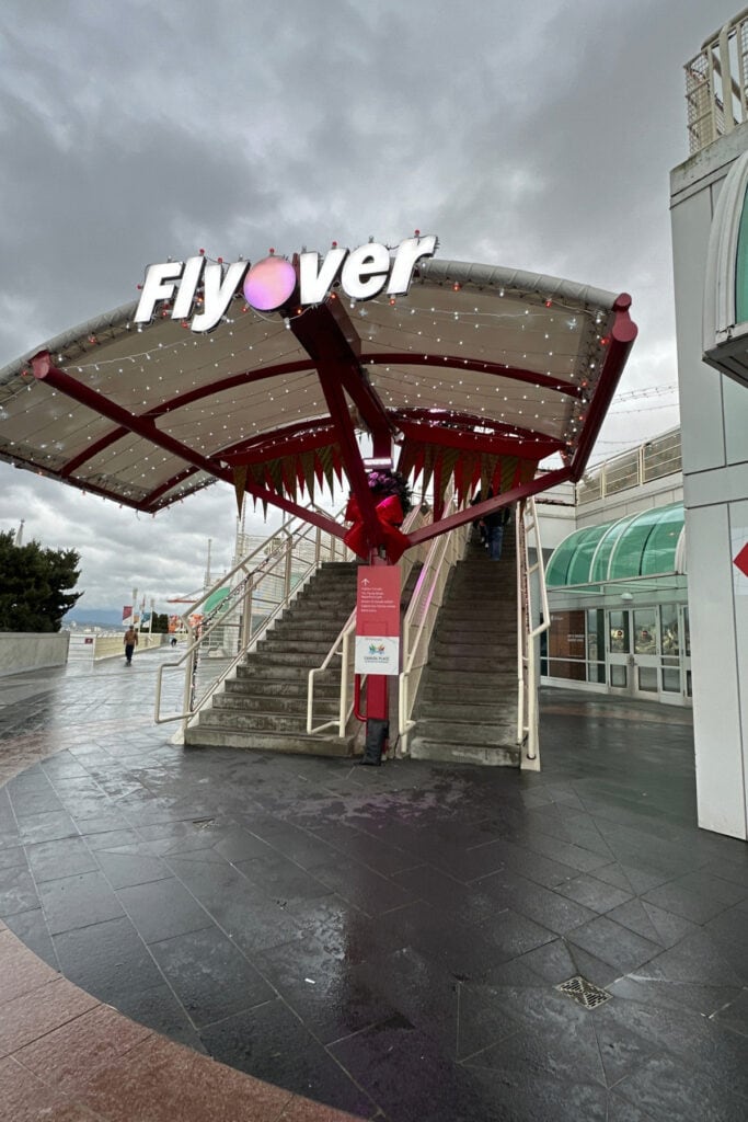 Flyover Vancouver entrance at Canada Place, with illuminated Flyover signage above an outdoor staircase decorated with holiday lights.
