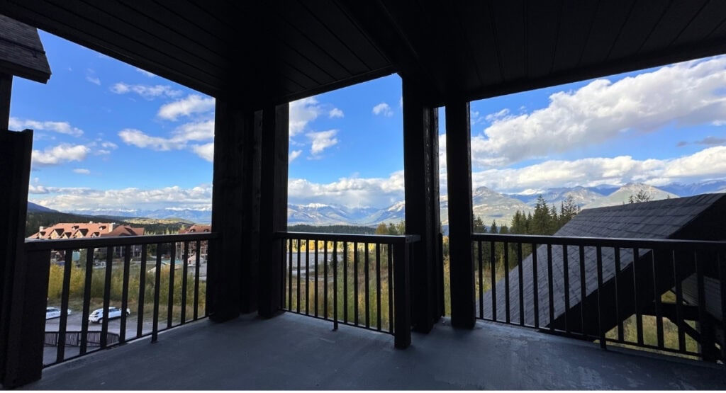 Covered balcony at Palliser Lodge near Golden, BC, overlooking Kicking Horse Mountain Resort buildings and distant mountains.