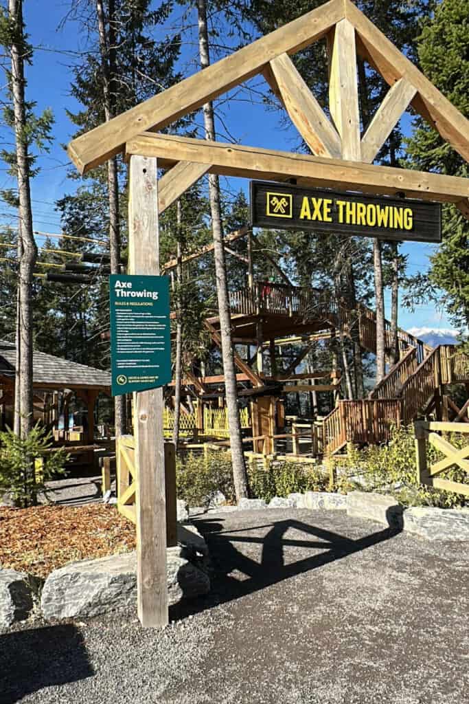 A wooden Axe Throwing sign marks the activity area at Golden Skybridge, with timber platforms, stairs and surrounding evergreen trees visible behind it. Axe throwing is one of the additional activities visitors can try at the attraction.