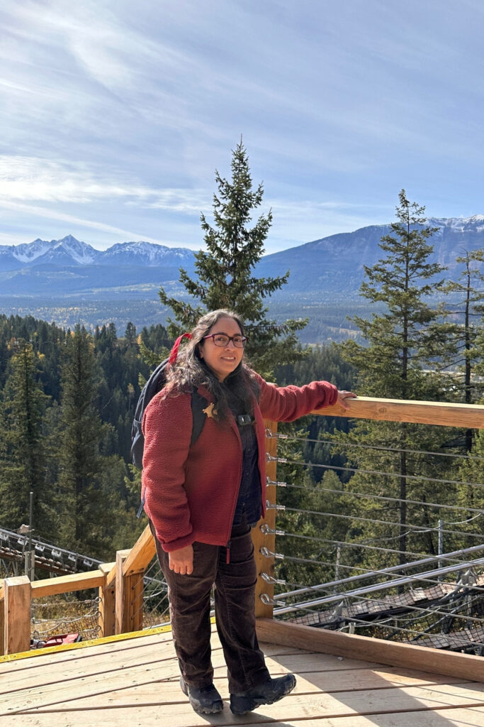 Travel writer standing on a wooden viewpoint at Golden Skybridge near Golden, BC, overlooking forested valleys and snow-dusted mountains.