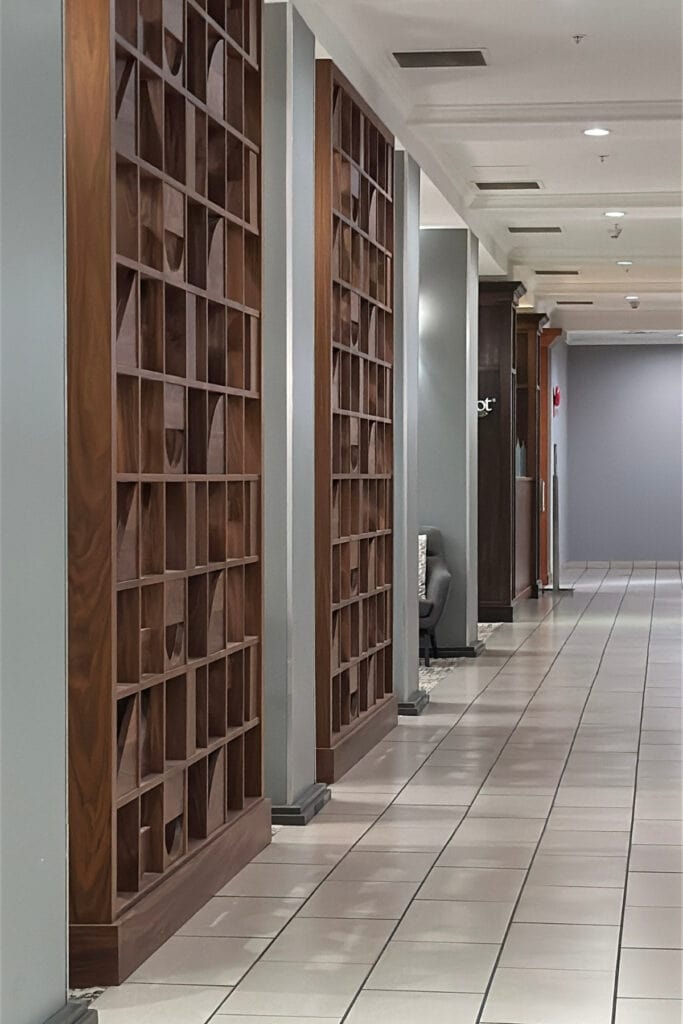 Long tiled hallway with geometric wooden partitions and recessed ceiling lights at Holiday Inn & Suites Kamloops, BC. The corridor leads past the hotel's lounge seating areas.
